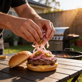 ACIDE Jalapeno Onions being piled onto an open beef burger by hand at a backyard barbecue
