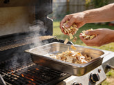 Western BBQ Products Apple Smoking Wood Chips lifestyle photo — loading apple wood chips into a smoker tray on the grill