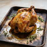 Whole roast chicken with golden crackling skin on a metal tray with pan juices