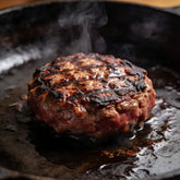 Thick beef burger patties with charred crust sizzling on a cast-iron griddle