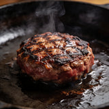 Thick beef burger patties with charred crust sizzling on a cast-iron griddle