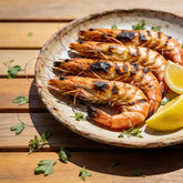 Grilled prawns with lightly charred shells on a plate with lemon wedges and herbs