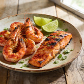 Grilled prawns and salmon with a reddish spice crust, plated with lime wedges