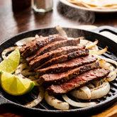 Sizzling skirt steak sliced for fajitas on a hot cast-iron platter with steam, lime wedges and charred onions