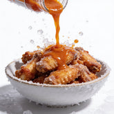 Atomic Chicken Buffalo Hot Sauce 250ml — sauce pouring over crispy fried wings, frozen mid-splash