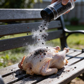 Atomic Chicken Charcoal Chicken Seasoning Rub 280g — seasoning shaken over a raw whole chicken, spice grains frozen mid-air