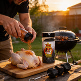 Atomic Chicken Charcoal Chicken Seasoning Rub 280g — man rubbing seasoning onto a raw whole chicken beside the rotisserie at sunset