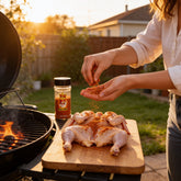 Atomic Chicken Chicken Peri Peri Seasoning Rub 200g — woman rubbing seasoning onto raw butterflied chicken beside the grill at sunset
