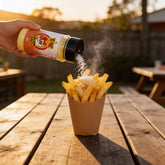 Atomic Chicken Chicken Salt Seasoning 330g — hot chips in a paper cone being showered with chicken salt at a backyard picnic table