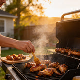 Atomic Chicken Honey Mango BBQ Sauce 250ml — hand brushing glaze onto wings on an outdoor grill at sunset