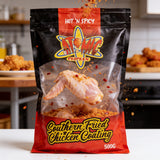 Atomic Chicken Hot 'N Spicy Southern Fried Chicken Coating 500g — raw wing frozen mid-air dropping into the spicy coating with chilli flakes flying