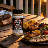 Boars Night Out White Lightning shaker beside grilled corn, chicken and whole fish on a rustic table