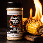 Close-up of charred grilled corn on the cob beside a Boars Night Out White Lightning shaker with fire glowing behind