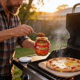 Chuck Hughes Spicy Antipasto 375ml antipasto condiment — spooning spicy antipasto from an open jar over a pizza on the barbecue