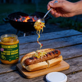 Chuck Hughes Spicy Mustard Coleslaw spooned onto a chargrilled sausage in a bun, open jar on the table