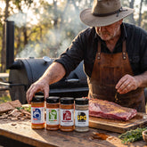 Chuds BBQ Range Bundle Texas rubs and seasonings — all four shakers on a prep bench as a pitmaster reaches for one at a cook