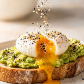 Coast n Smoke Bancoora Bagel seasoning — a poached egg cut open with golden yolk flowing under a shower of seeds