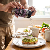 Coast n Smoke Bancoora Bagel seasoning — person sprinkling the seeded seasoning over avo toast and eggs at the table