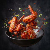 Coast n Smoke K-Pop Dust Korean BBQ — lacquered Korean chicken wings caught mid-toss with sesame scattering