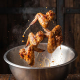 Coast n Smoke Winki-POP Dust — crisp chicken wings caught mid-toss in a bowl, glossy skin glistening