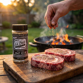Elk Creek Black Label A-P all-purpose rub — raw ribeye steaks being seasoned on a board by a charcoal grill