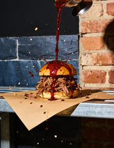 Fancy Hank's Original BBQ Sauce pouring over a pulled pork brioche bun