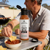 A person spooning Flavour & Spice Aztec Tomato Relish onto a plate of sausages and chips