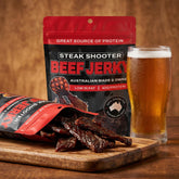 Low n Slow Basics Steak Shooter beef jerky — dark beef jerky strips spilling from the pack beside a cold beer