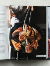 Meat Illustrated by America's Test Kitchen hardback cookbook — spread of cast-iron lamb chops being turned with tongs