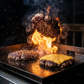 Middle Kingdom Beef Baron 165g beef seasoning — seasoned beef burger patty caught mid-flip over a hot flat-top with flame flare