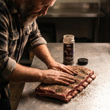 Middle Kingdom Beef Berserker 170g steak and brisket seasoning — pitmaster rubbing the seasoning into raw beef short ribs on a steel bench