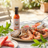 Nomad Chilli Co Watermelon & Lemon Myrtle hot sauce — barbecued whole fish and prawns drizzled at a summer table