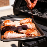 Seasoning raw chicken drumsticks with Plowboys Yardbird Rub beside the smoker