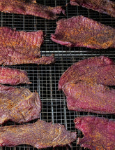 The MeatEater Outdoor Cookbook by Steven Rinella hardback cookbook — Ancho Cola Jerky drying on a rack