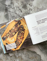 The New Camp Cookbook by Linda Ly hardback cookbook — open spread of bacon-wrapped trout stuffed with herbs