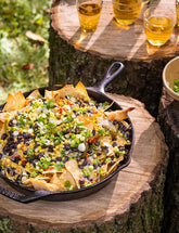 The Outdoor Cook by America's Test Kitchen paperback cookbook — loaded nachos in a cast-iron pan