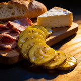 ACIDE Bread & Butter Zucchini Pickles served on a charcuterie board with roast pork, washed rind cheese and crusty bread