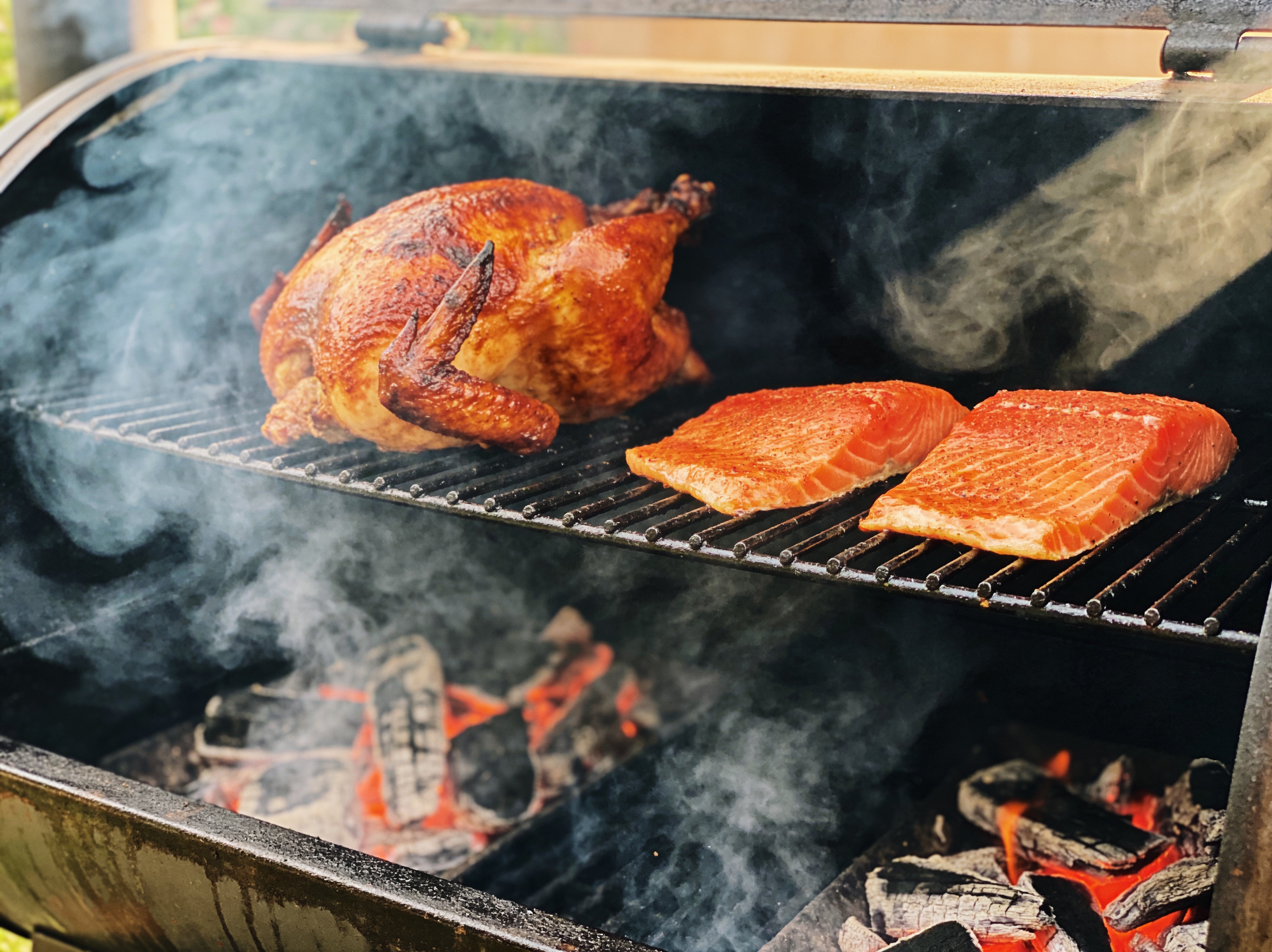 Western BBQ Products Cherry Smoking Wood Chips lifestyle photo — chicken and salmon smoking over cherry wood on the grill