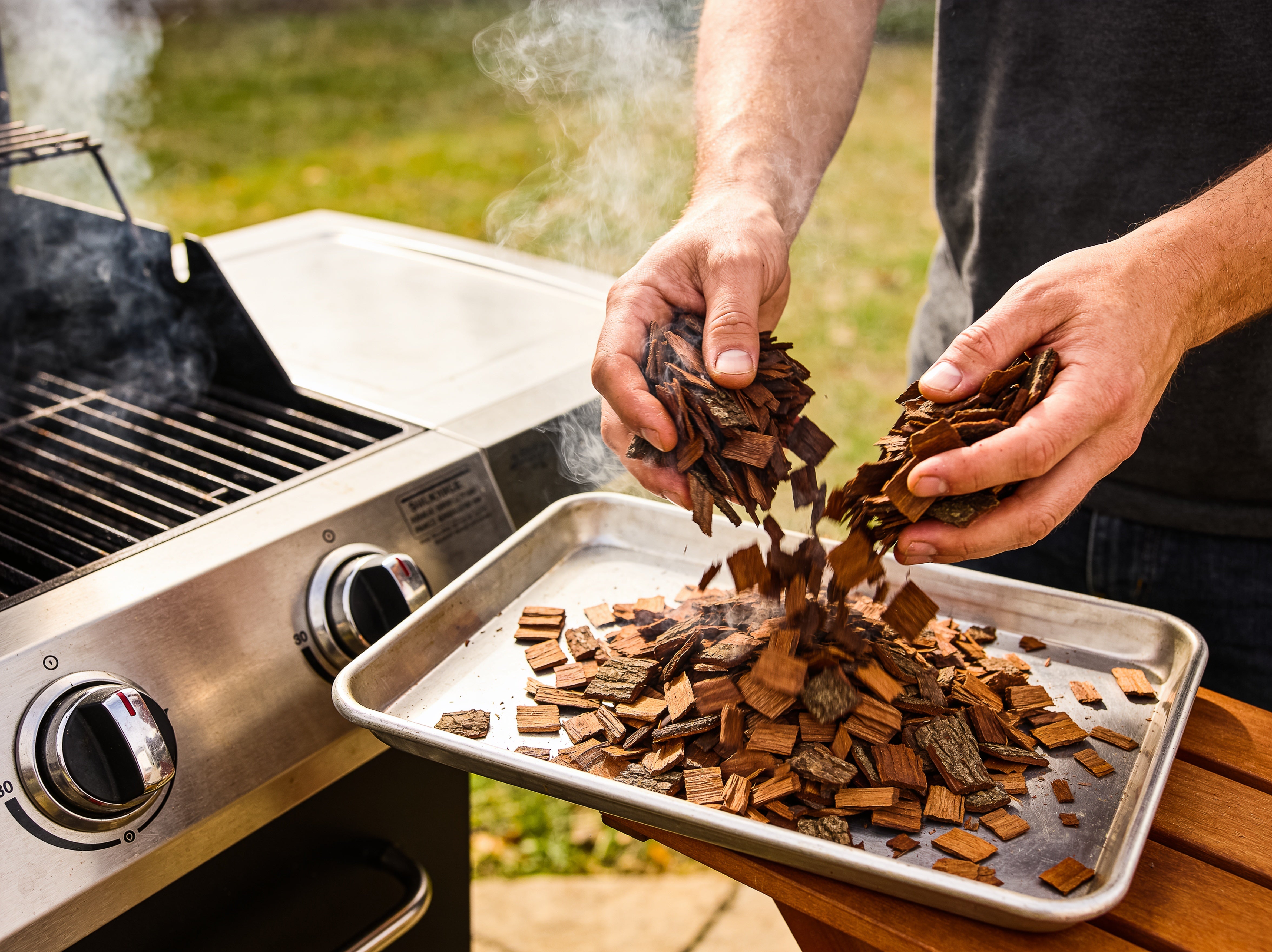 Western BBQ Products Hickory Smoking Wood Chips lifestyle photo — loading hickory wood chips into a smoker tray on the grill
