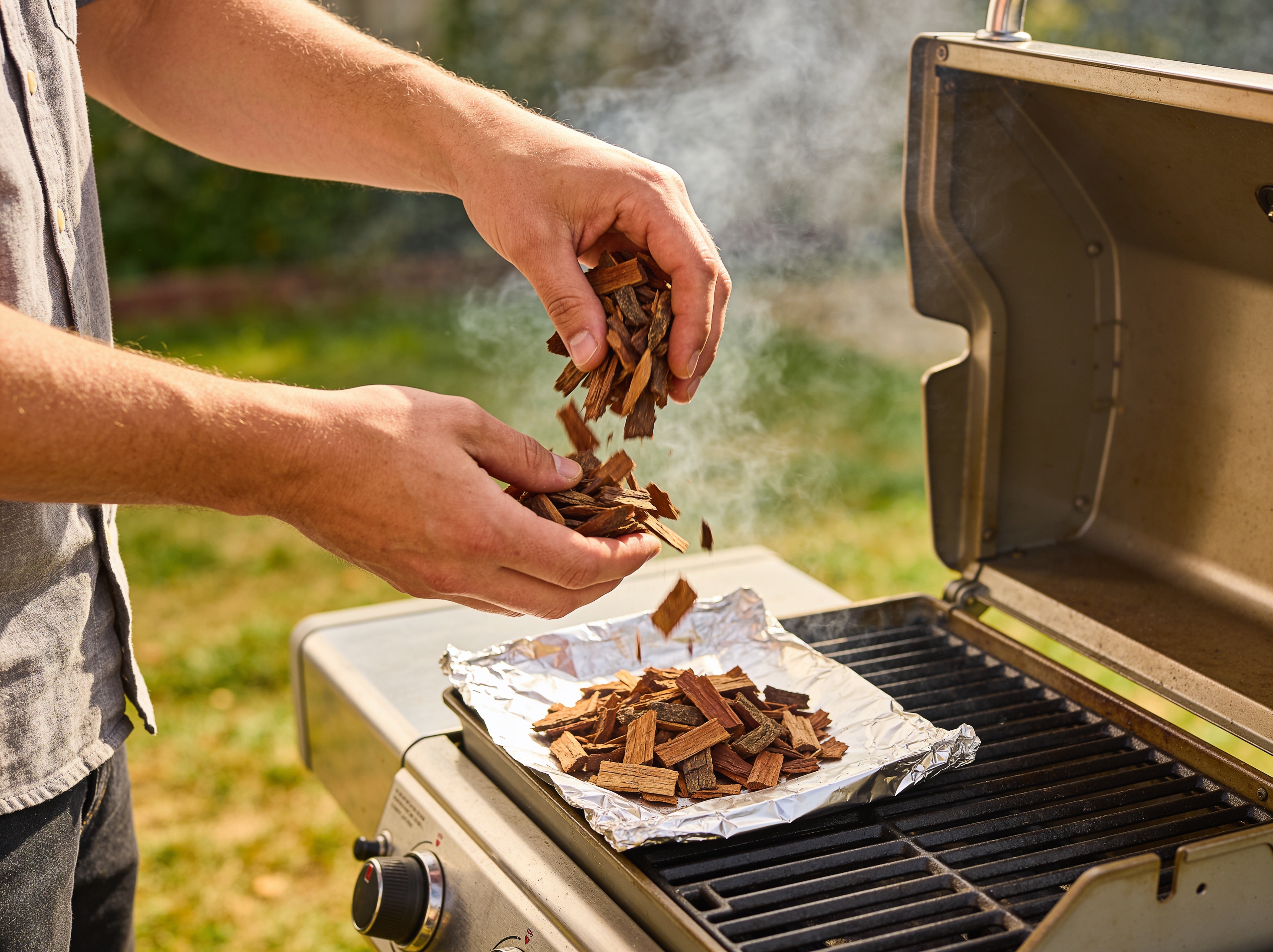 Western BBQ Products Mesquite Smoking Wood Chips lifestyle photo — loading mesquite wood chips into a foil smoker pouch on the grill