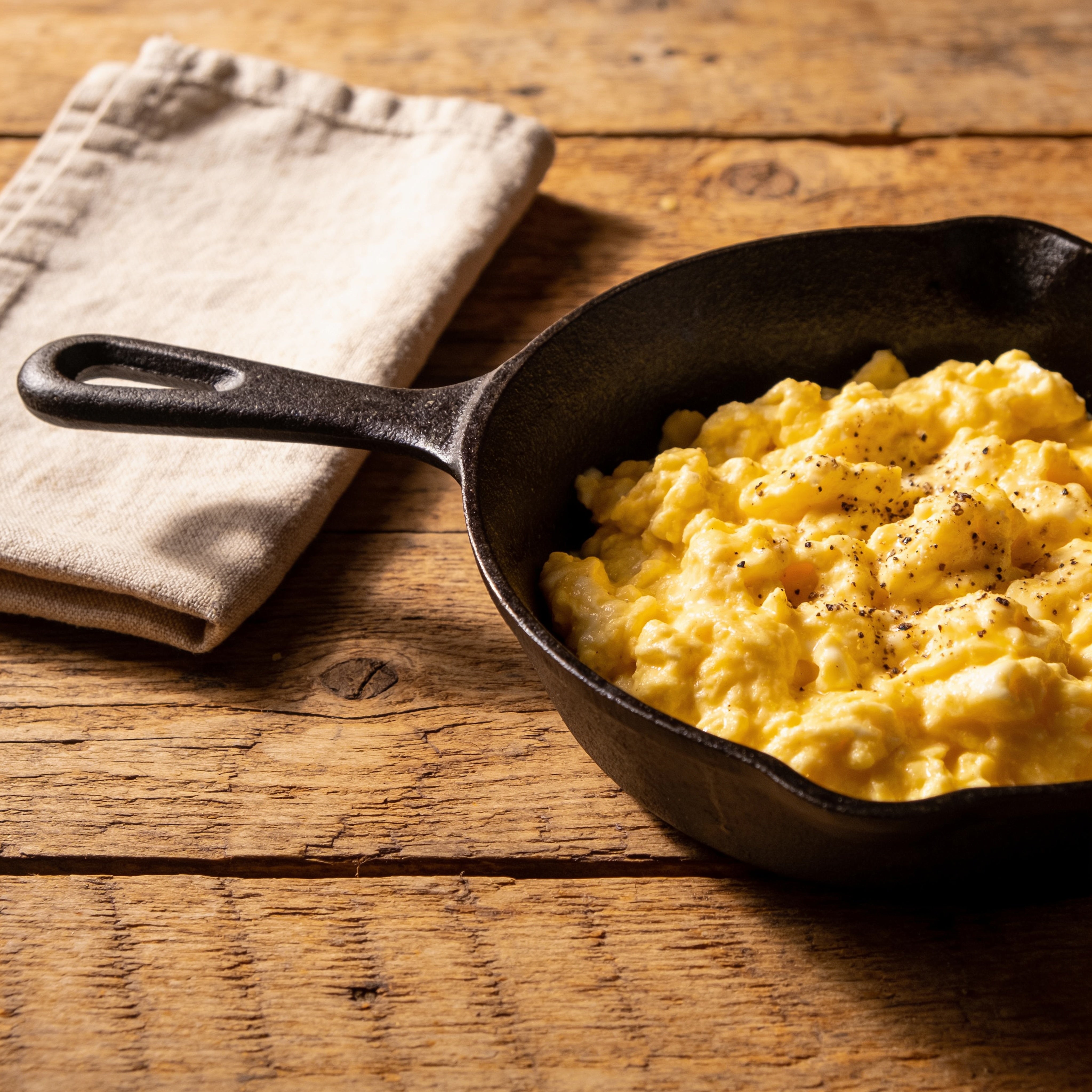 Skillet of soft scrambled eggs with cracked black pepper on a rustic wooden table