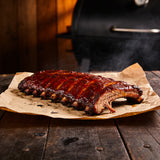 Smoked pork ribs with a glossy reddish bark resting on butcher paper