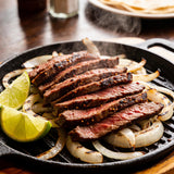 Sizzling skirt steak sliced for fajitas on a hot cast-iron platter with steam, lime wedges and charred onions