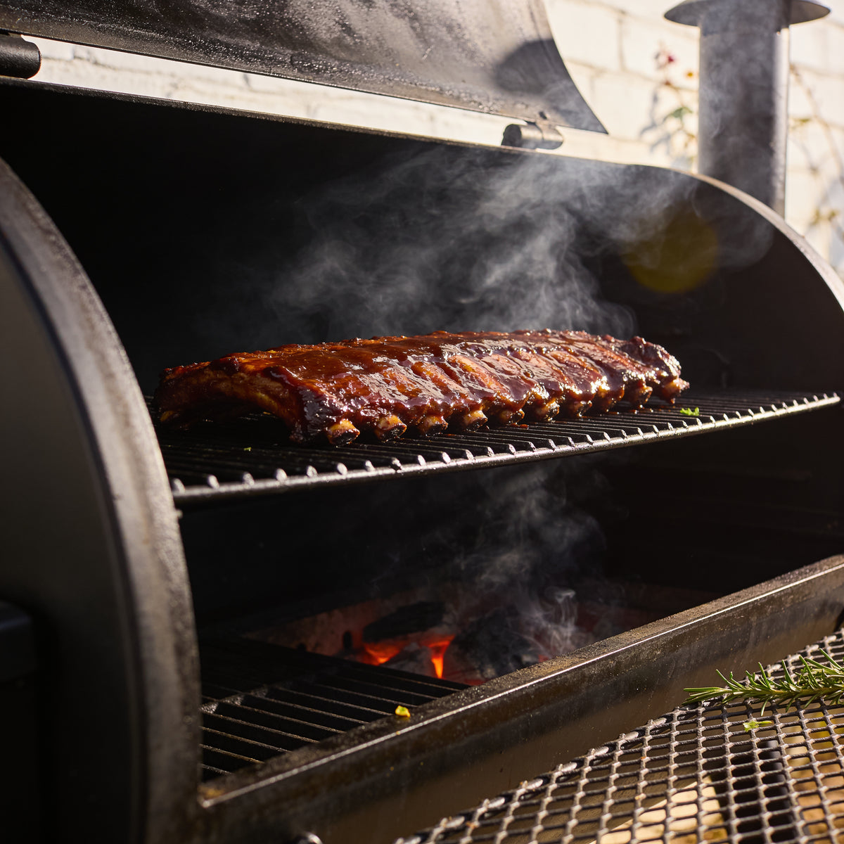 Ribs on the smoker grate coated in glossy dark caramel-brown lacquer