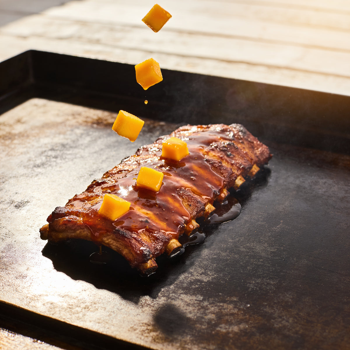 Macro garnish-drop of diced mango falling onto glazed pork ribs