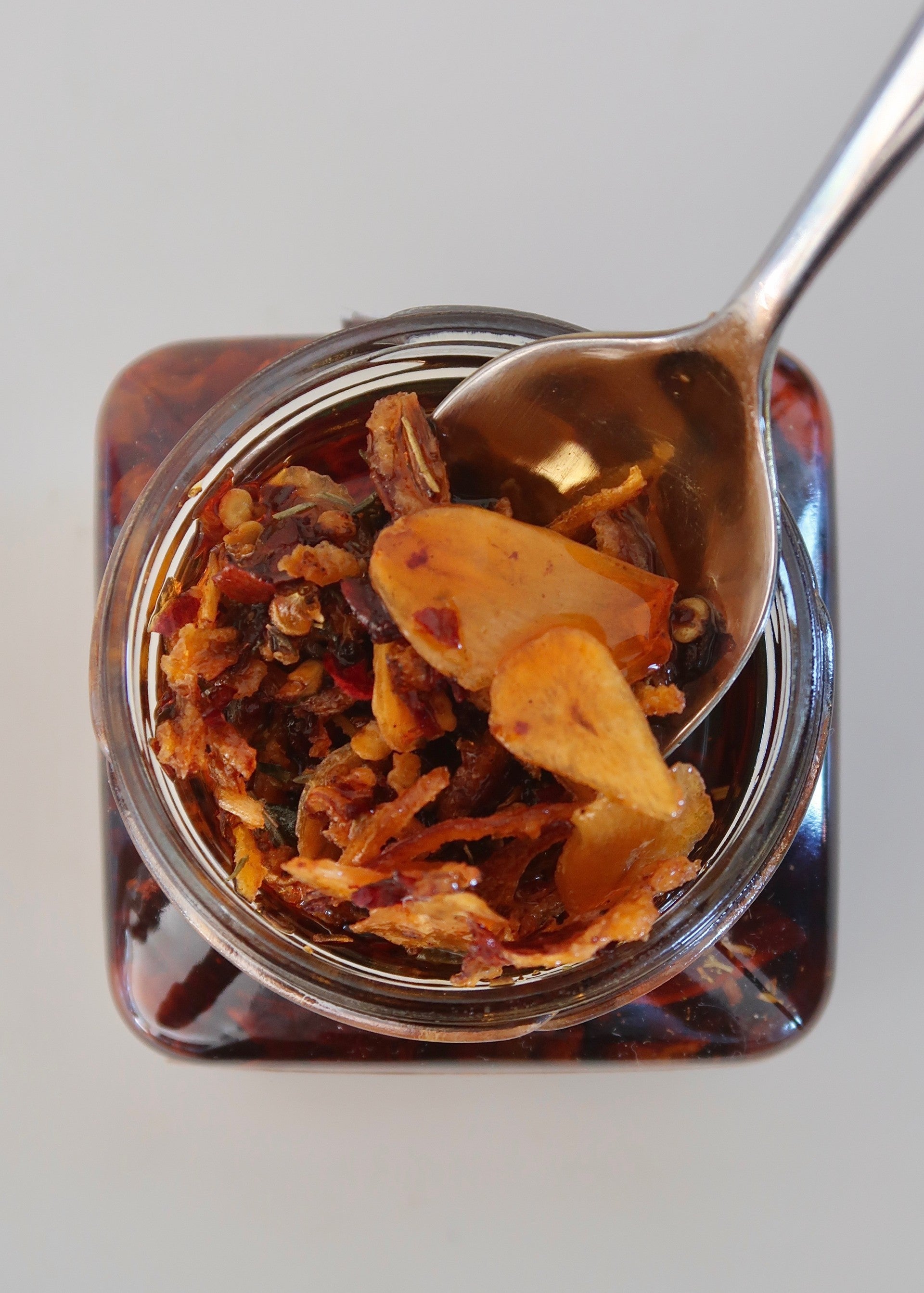 Nonna Piccante Chilli Oil jar with a spoon lifting crispy chilli, shallot and porcini from the oil