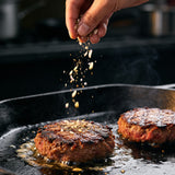 Bangin Burger Box - burger salt being showered over smash patties searing on a hot cast iron flat top