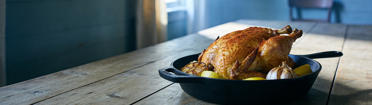 Golden roast chicken seasoned with BBQ Mafia The Snitch BBQ Rub in a cast-iron pan on an oak table