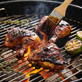 Big Jerk Energy box - jerk chicken thighs charring over charcoal being basted with dark glossy jerk marinade