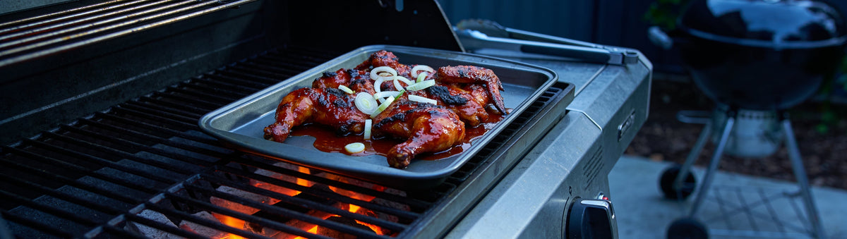 Hot BBQ Sauce glazed chicken wings on a tray over a charcoal grill at night